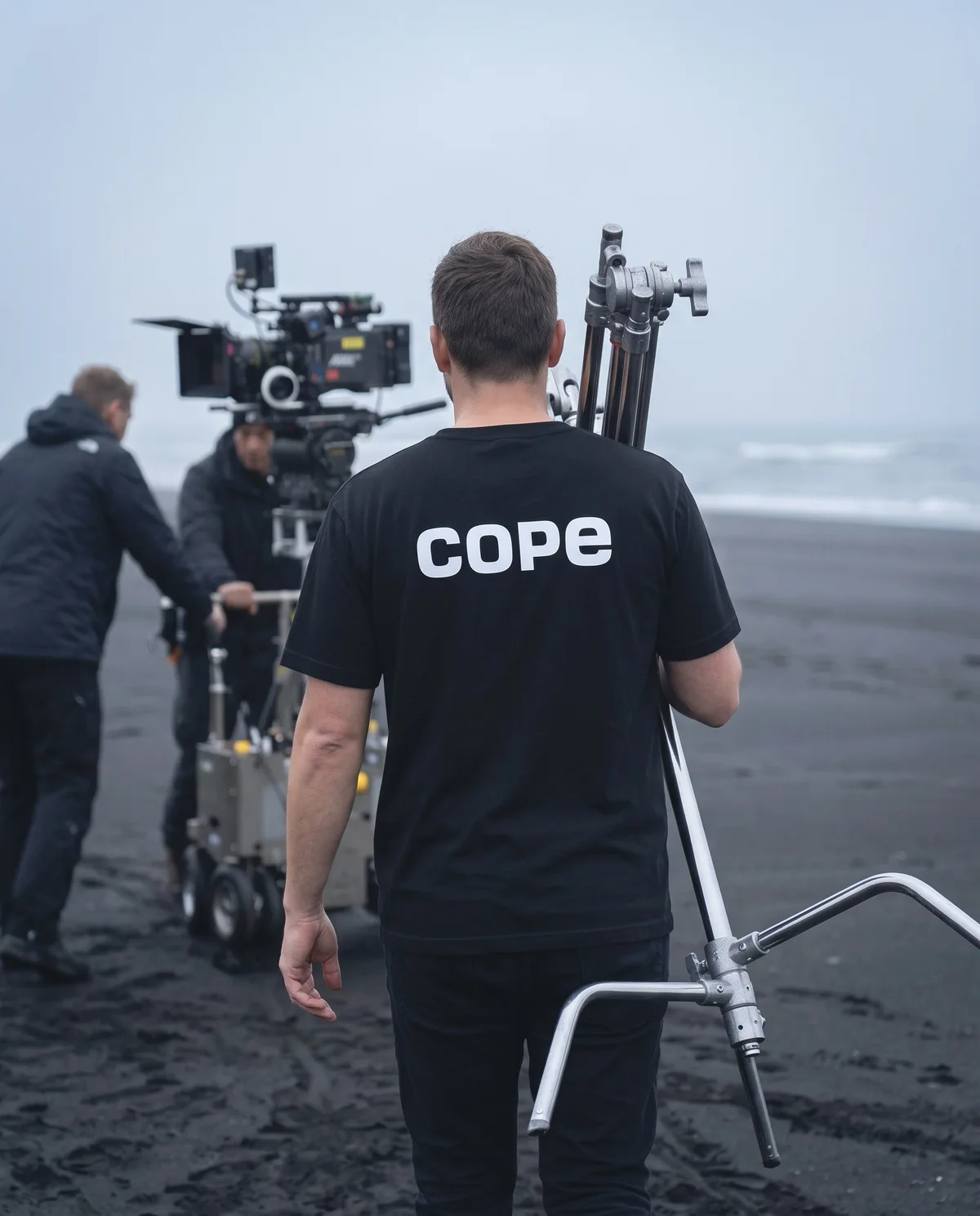 Grip on a black sand beach film set wearing the cope logo heavyweight t-shirt, back view