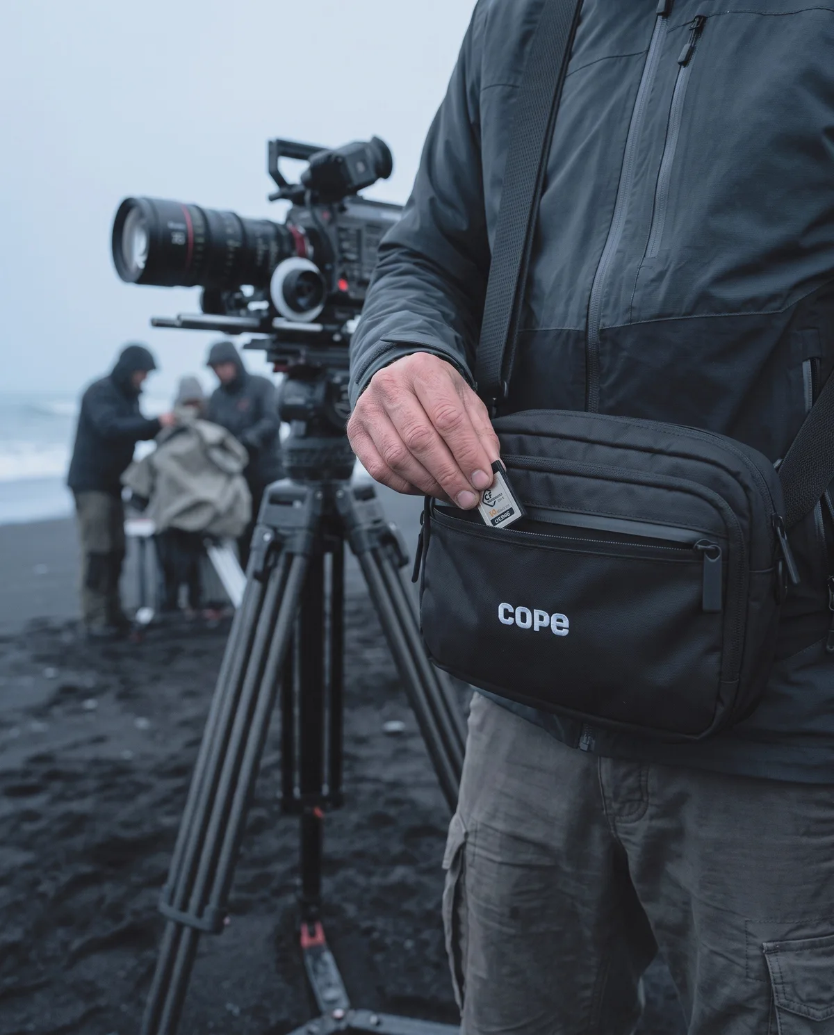 Camera assistant on a black sand beach film set wearing the cope logo crossbody bag