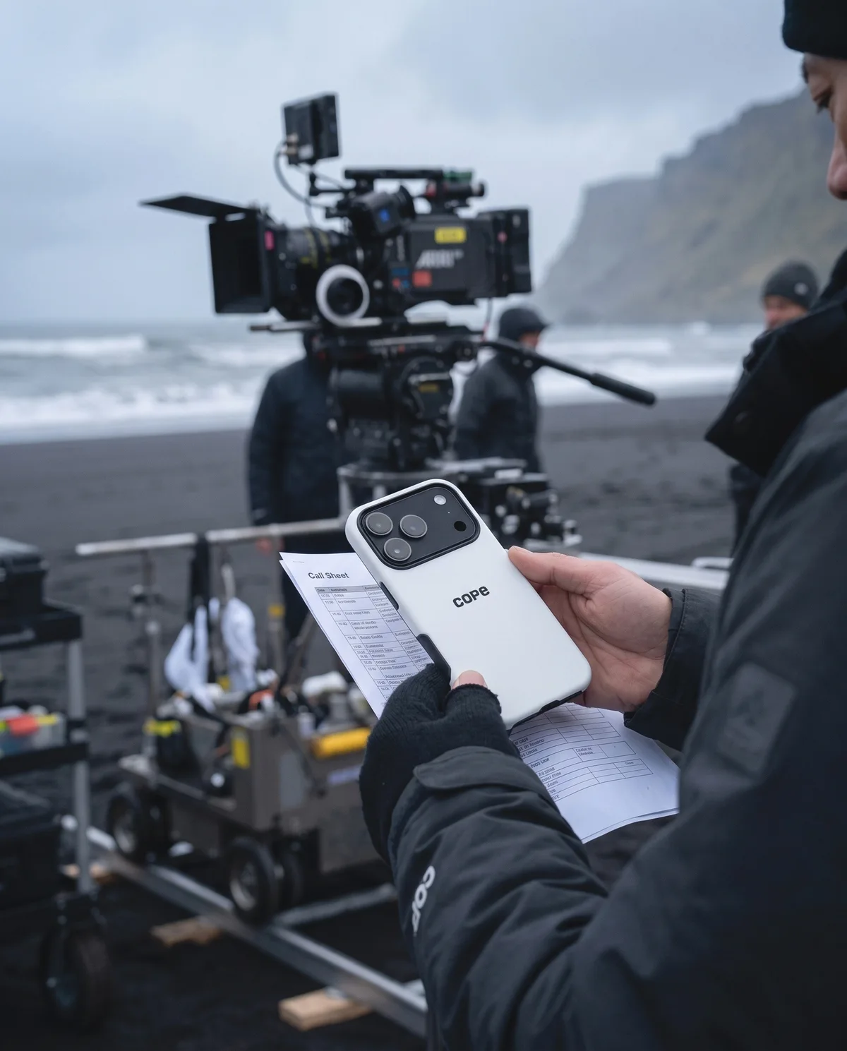 Crew member on a black sand beach film set holding an iPhone in the cope logo case