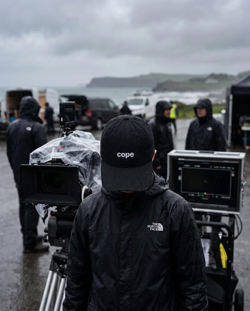 Crew member on a rainy film set wearing the cope cap with the small front logo